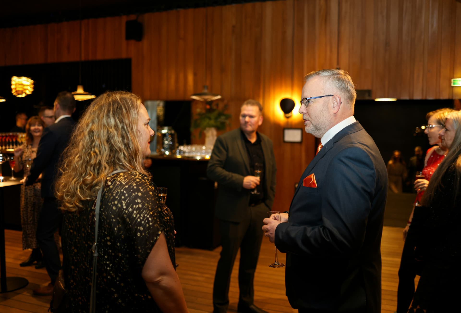 Professionals mingling with drinks at a formal business event.